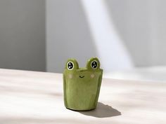 a small green frog figurine sitting on top of a wooden table next to a white wall