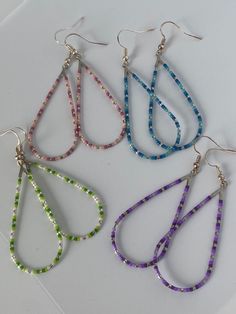 four pairs of dangling earrings with multicolored beads and silver earwires on a white surface