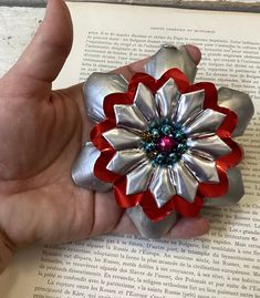 a hand holding a silver and red flower brooch on top of an open book