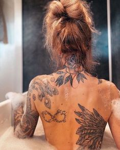 a woman with tattoos on her back sitting in a bathtub