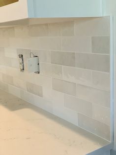 a kitchen counter with white tile on the backsplash and an outlet in the wall