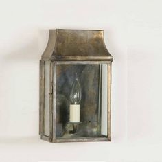 an old fashioned wall mounted lantern with a candle in it's glass case on a white wall