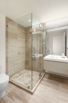 a bathroom with a toilet, sink and glass shower stall in the middle of it