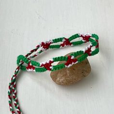 two bracelets with red, white and green beads are sitting next to a rock