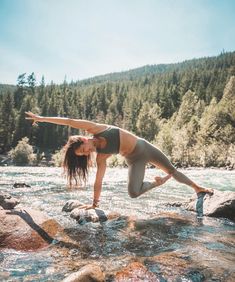 a woman is doing yoga on rocks in the middle of a river with trees behind her