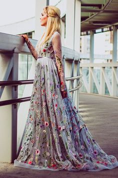 a woman in a long dress leaning against a railing looking off into the distance with her hands on her hips