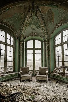 two chairs sitting in an old room with broken windows and debris all over the floor