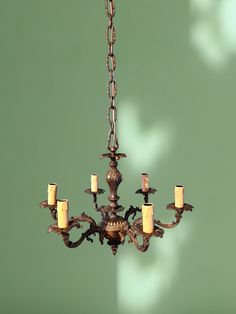 a chandelier with five lit candles hanging from it's center, in front of a green wall