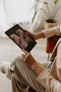 a woman sitting in a chair holding an electronic device with her face on the screen