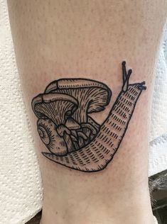 a black and white tattoo of a snail on the ankle with a small piece of bread in it