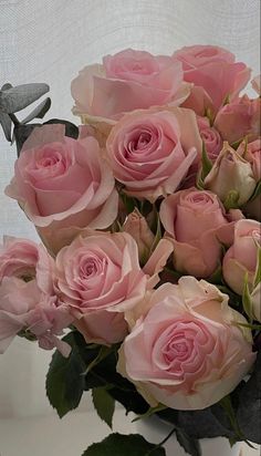 a vase filled with lots of pink roses on top of a white tableclothed surface