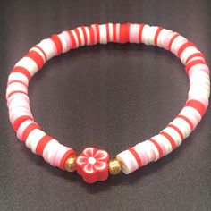 a red and white beaded bracelet on a black surface with gold accents, beads and flowers