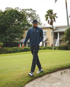 a man walking across a green covered golf course next to a house and palm trees