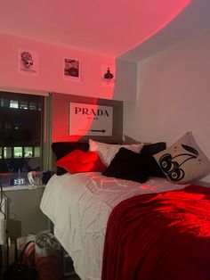 a bed with red sheets and pillows in a room that has pink lighting on the walls