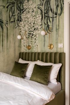 a bed with white sheets and pillows in front of a green wallpapered headboard