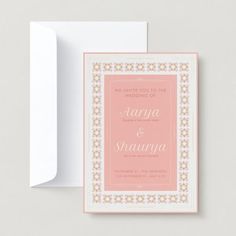 a pink and white wedding card on top of a envelope