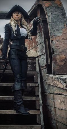 a woman dressed in black and white standing on steps with a pirate ship behind her