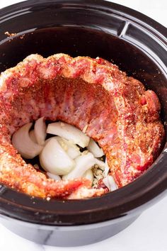 an open crock pot filled with meat and onions on top of a white table