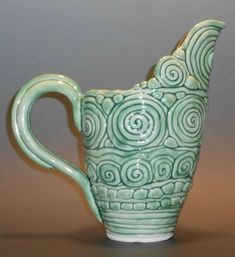 a green and white ceramic pitcher sitting on top of a wooden table next to a gray wall