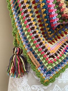 a multicolored crocheted blanket with tassels hanging from the back