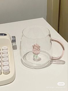 a glass cup with a rose on it next to a calculator and cell phone