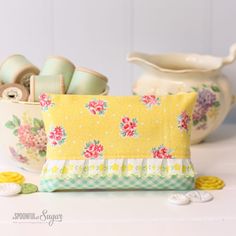 a yellow flowered pillow sitting on top of a table next to some sewing supplies