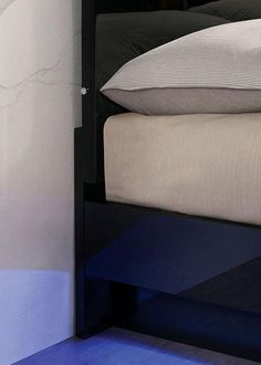 a night stand with two pillows on top of it next to a bed and wall