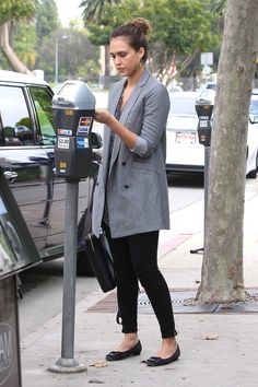 a woman standing next to a parking meter on the side of a street with her hand in her pocket