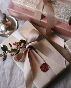 two wrapped gift boxes with ribbons tied around them on a table next to candles and flowers