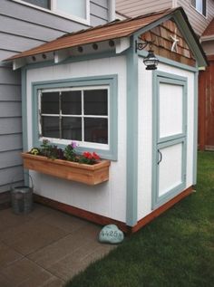 a white and blue shed with flowers in the window sill next to a house