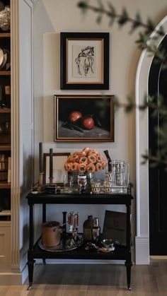 a black table topped with lots of bottles and glasses next to a wall filled with pictures