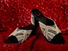 a pair of black and white slippers sitting on top of a red cloth covered bed