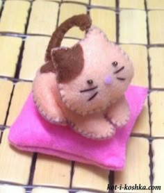 a small stuffed cat sitting on top of a pink towel with a brown head and tail