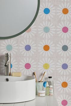 a bathroom sink sitting under a mirror next to a wall paper with colorful dots on it