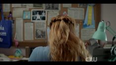 the back of a woman's head with long hair in a messy ponytail sitting at a desk