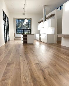 an empty living room with wood floors and white cabinets in the background is a large open kitchen