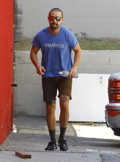 a man in blue shirt and brown shorts walking down the street with his hands on his hips