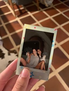 a person holding up a polaroid with two girls on it in front of a tiled floor