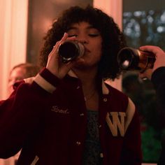 a woman drinking from a mug while standing next to another woman in a red jacket