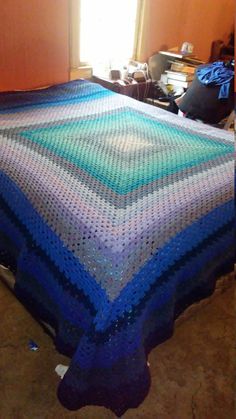 a bed with a blue and green crocheted blanket on it