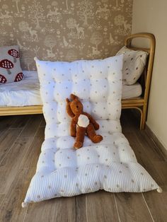 a brown teddy bear laying on top of a white pillow next to a wooden bed