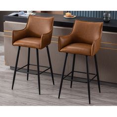 two brown leather bar stools sitting next to each other on top of a kitchen counter