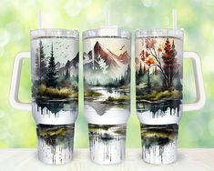 three travel mugs with mountains and trees painted on them, sitting on a table