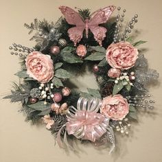 a wreath with pink flowers and butterflies hanging on the wall next to a white wall