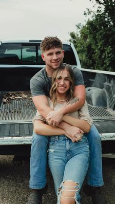 a man and woman sitting on the back of a pick up truck with their arms around each other