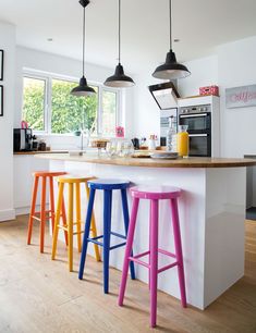 three colorful stools sit in front of an island counter with two yellow and one pink barstools