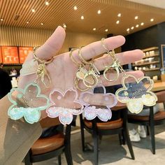 a hand holding five different colored keychains in front of a table with chairs