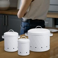 a woman standing next to three white canisters on top of a wooden counter