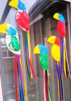 three colorful paper birds hanging from a window sill with streamers in the shape of parrots