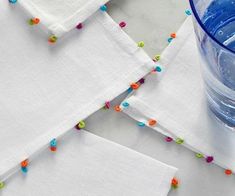 four white napkins with colorful beads on them next to a blue cup and water